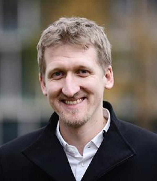 a person in a white collared shirt and black coat smiling at the camera