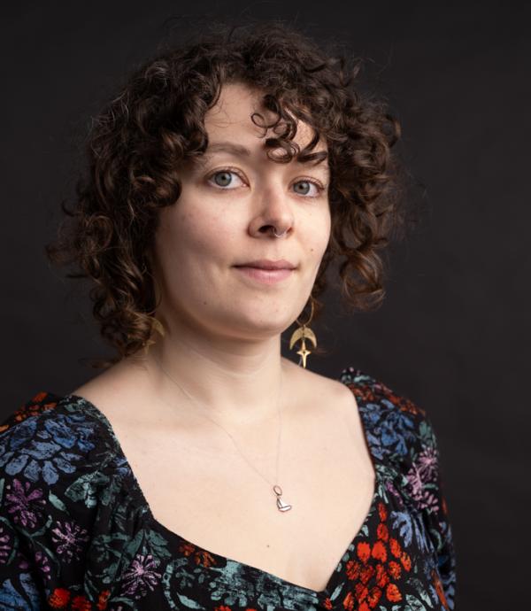 A person with curly hair and a floral dress in front of a dark background